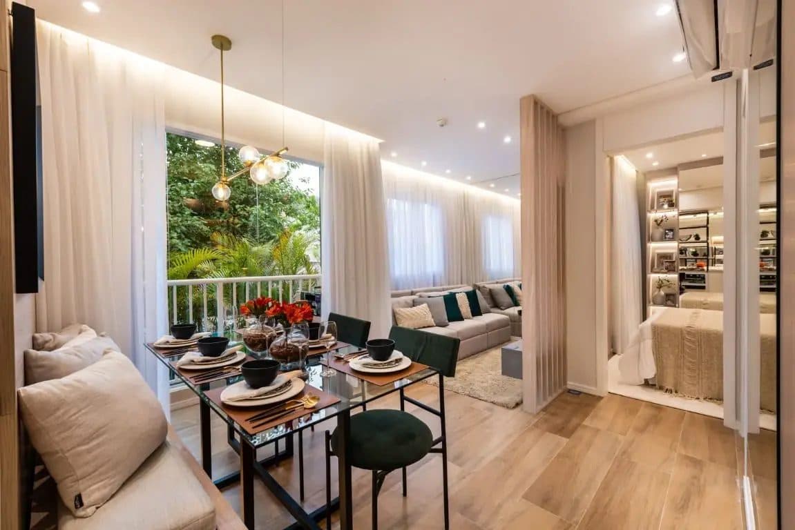 Sala de jantar integrada com sala de estar, com mesa de vidro, cadeiras estofadas e vista para área verde.